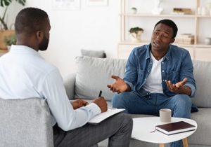 man sitting on couch talking to a therapist in a trauma therapy session