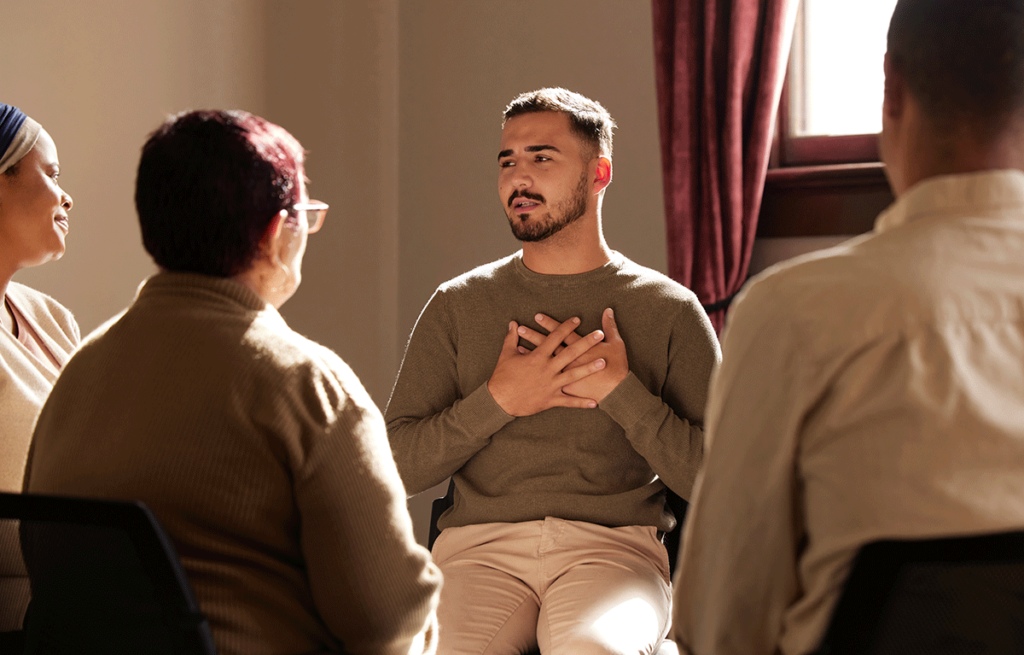 man learning about different types of group therapy touches hands to his chest