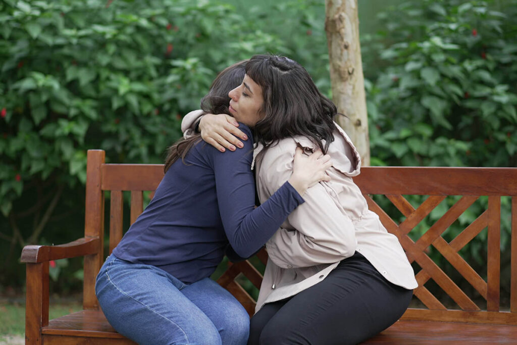 two people hugging on park bench after one of them learned how to help your friend during relapse
